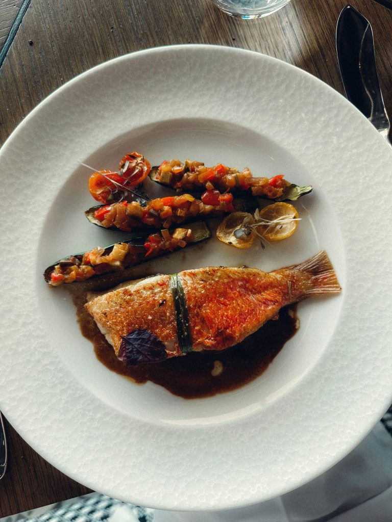 Top view of a gourmet fish dish served with stuffed zucchini and sauce on a white plate.